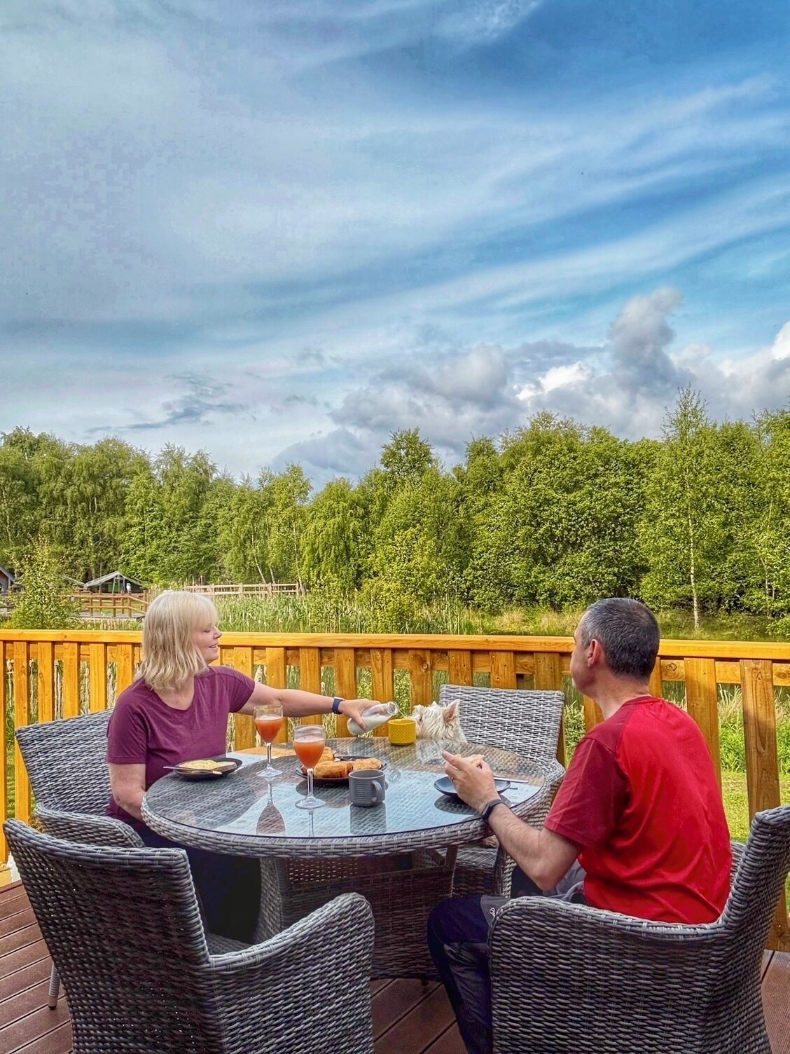 Una mesa redonda con sillas de mimbre en una terraza al aire libre, rodeada de follaje.