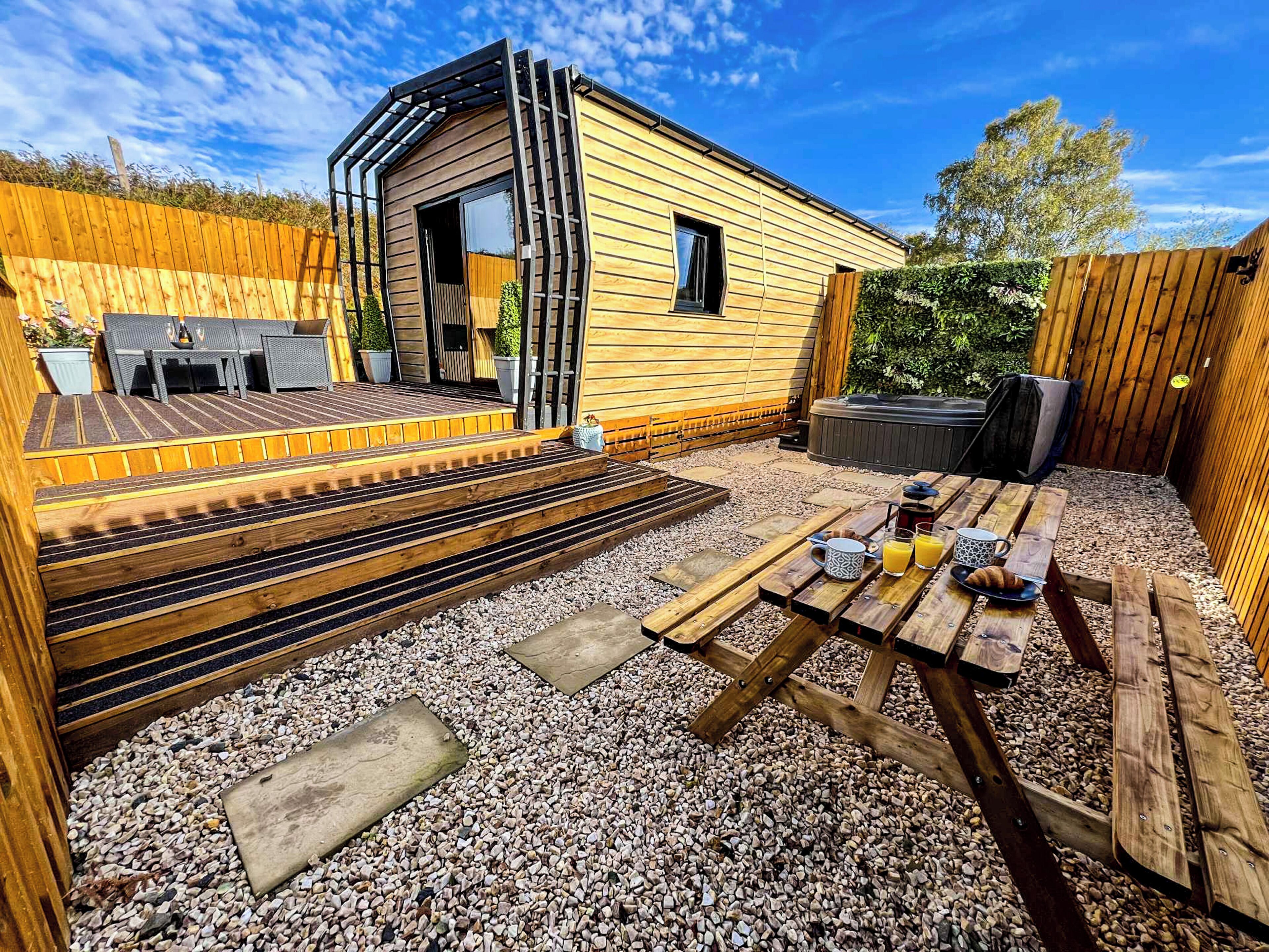 A wooden cabin with a patio, outdoor seating, and a hot tub.