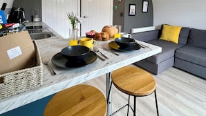 A modern kitchen with a marble countertop, two stools, a dining table, and a sofa with a yellow pillow. - Newmore Highland Pods (Invergordon)