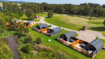 A series of dome-shaped cabins with outdoor seating, surrounded by a grassy field and a small body of water.