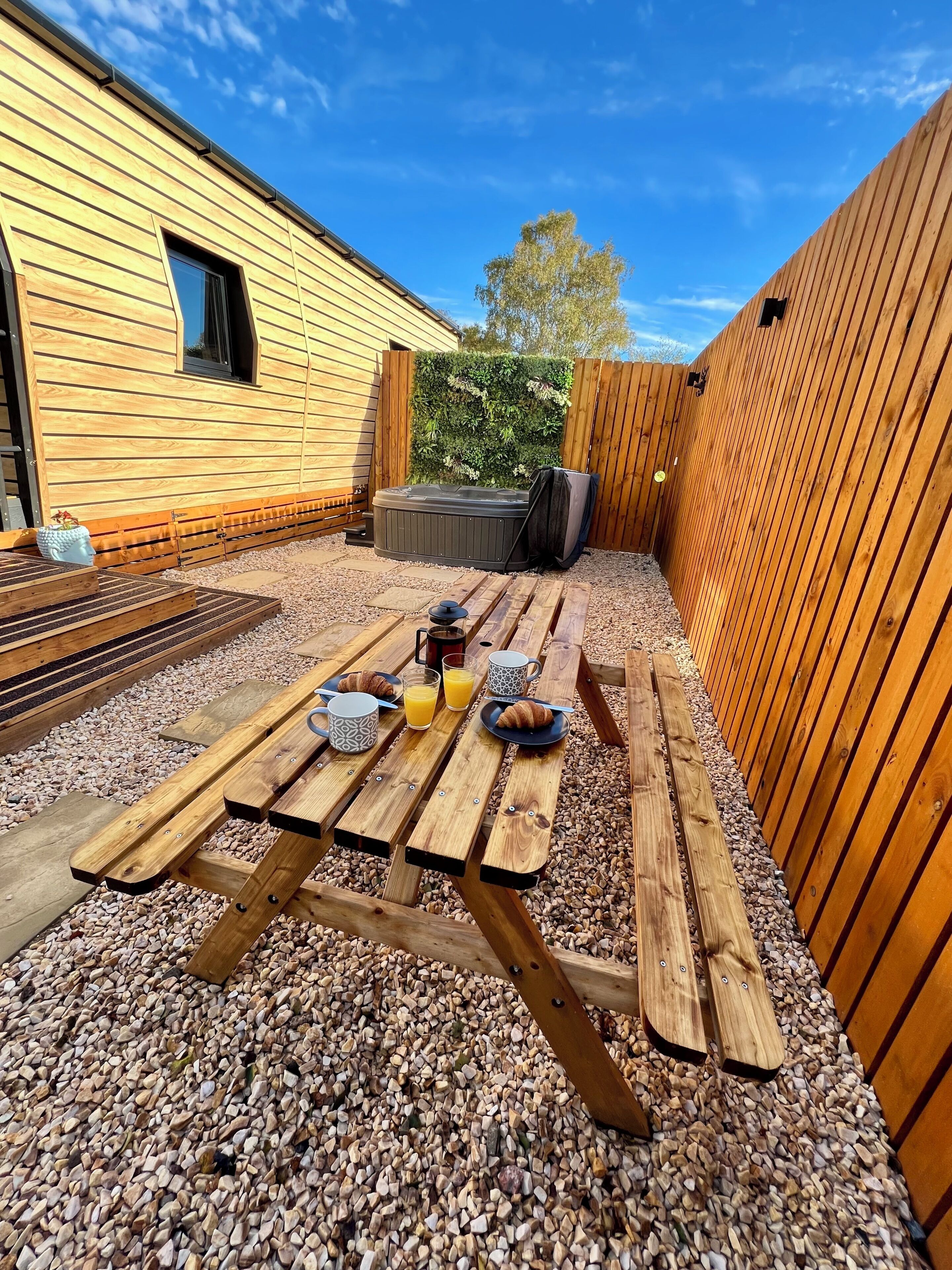 A wooden deck with picnic tables, a hot tub, and a wooden fence.