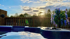 A hot tub with a wooden fence and a flowering plant in the background. - Newmore Highland Pods (Invergordon)