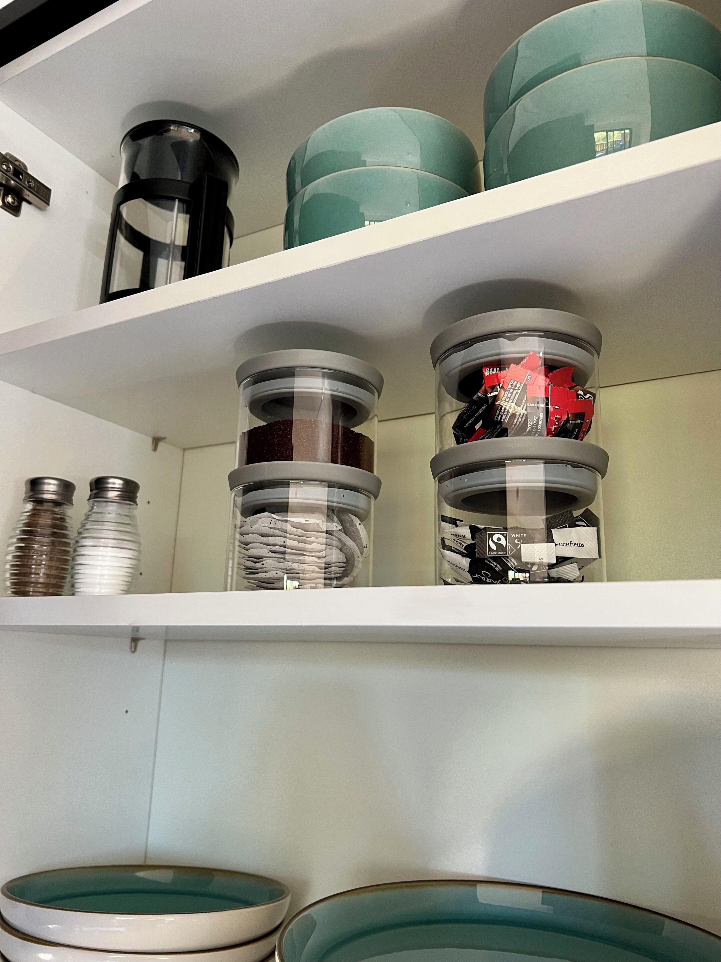 A kitchen shelf with storage containers, a coffee maker, and a spice rack.