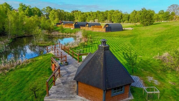A rural property with a pond, wooden deck, and several barns. - Newmore Highland Pods (Invergordon)