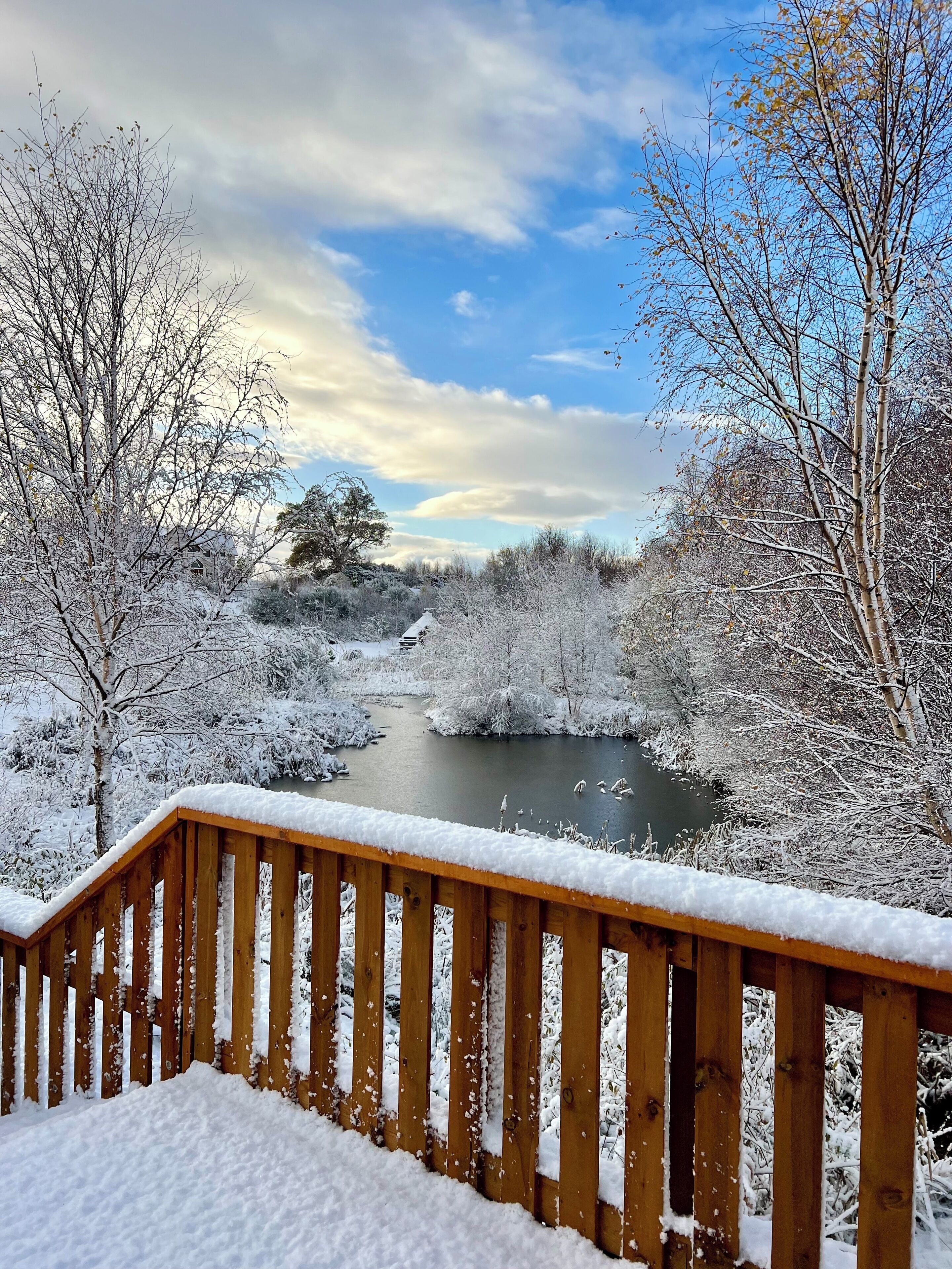 Una terraza de madera cubierta de nieve, un río y árboles circundantes.