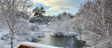 Una terraza de madera cubierta de nieve, un río y árboles circundantes.