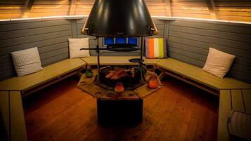 A cozy room with a central wood-burning stove, benches, and a sloped ceiling with lighting.
