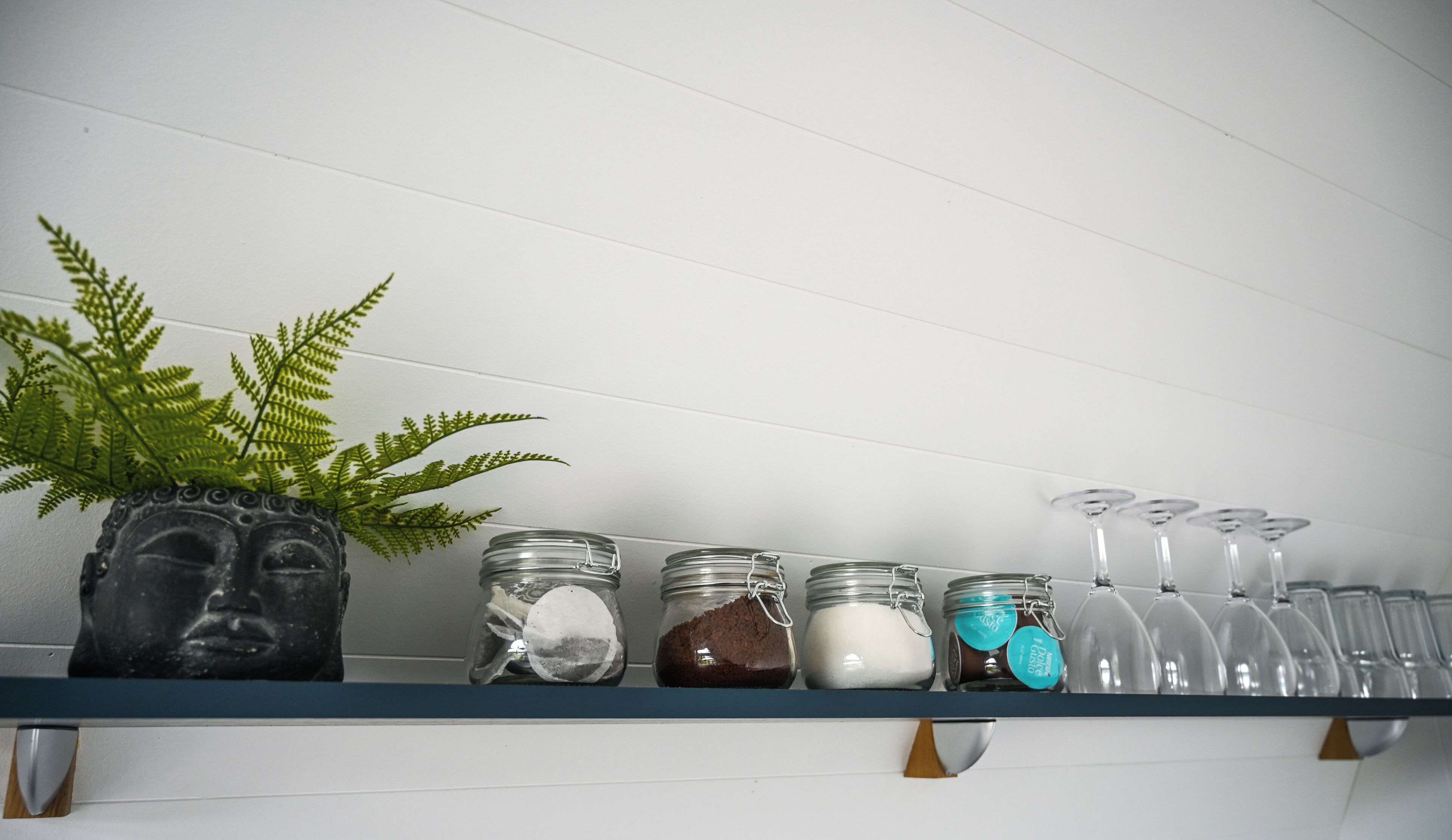 A shelf with a Buddha head sculpture, a fern, and jars of spices.