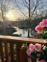 A wooden deck overlooking a calm lake with trees and a clear sky.