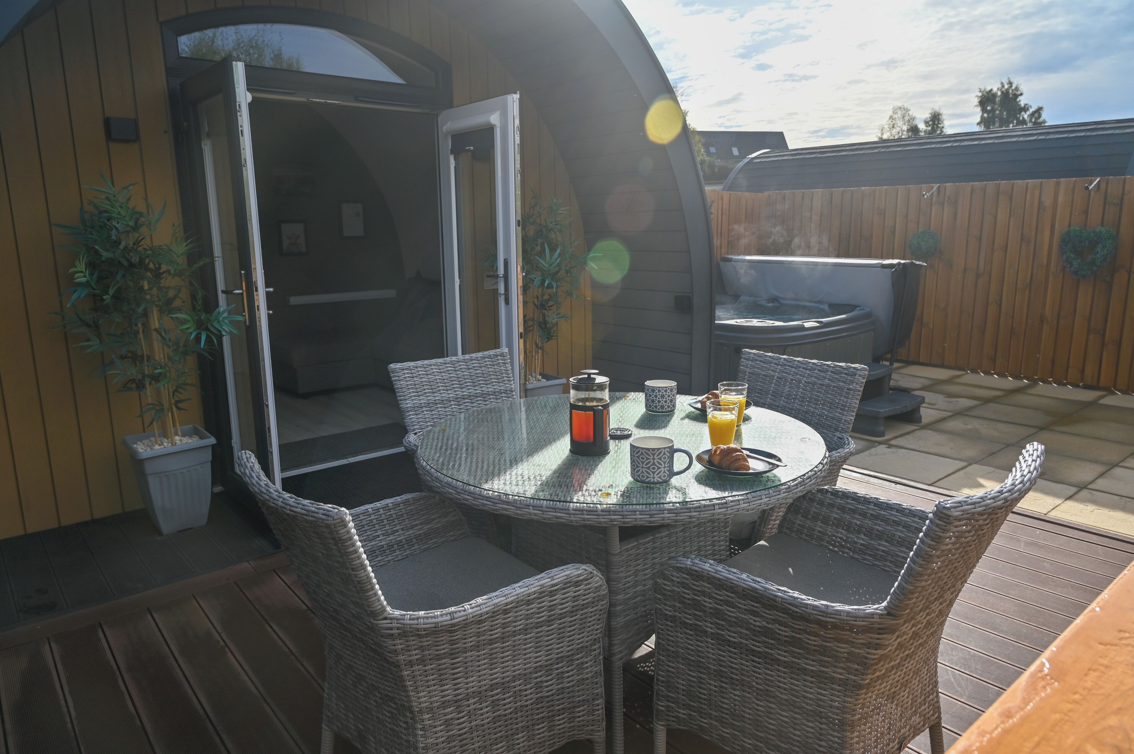 An outdoor patio with wicker furniture, a glass table, and a hot tub.