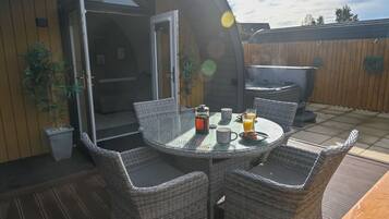 An outdoor patio with wicker furniture, a glass table, and a hot tub.