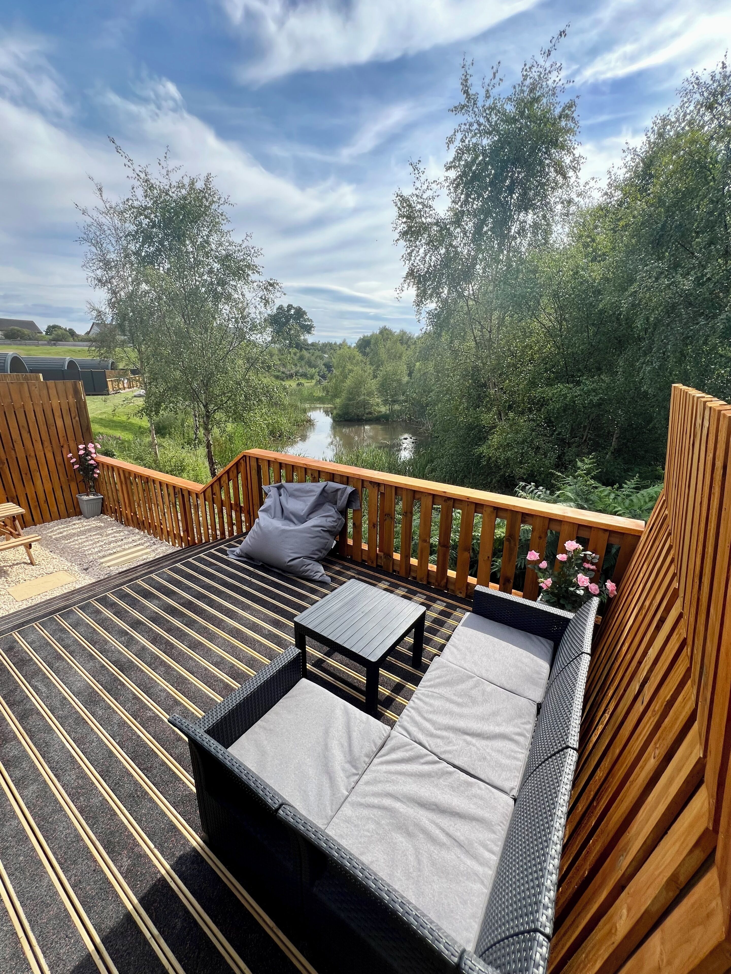A deck with a sofa, a small table, and a view of a river and greenery.