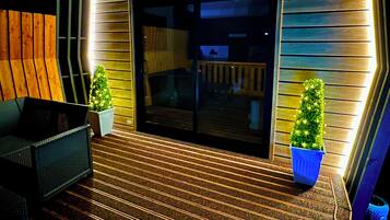 A deck with a wooden floor, a black sofa, and two potted plants.