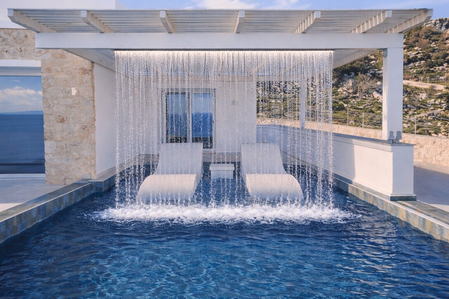 Ein Pool mit Wasserfall, einer Steinmauer und Blick auf das Meer.