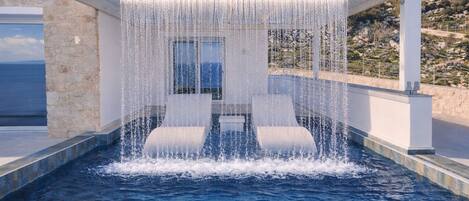 Ein Pool mit Wasserfall, einer Steinmauer und Blick auf das Meer.