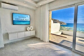 A modern interior with a TV displaying 'Welcome to AQUA BLUE VILLA,' a balcony with a sea view, and a minimalist design. - Villa 'Aqua Blue 2' with Private Pool and Sea View (Amoopi)
