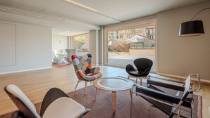 Un interior moderno con un ventanal grande, una silla negra, una silla blanca, una silla colorida y una mesita redonda.