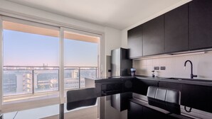 Una cocina moderna con encimera negra, electrodomésticos de acero inoxidable y vistas a la ciudad a través de amplios ventanales.