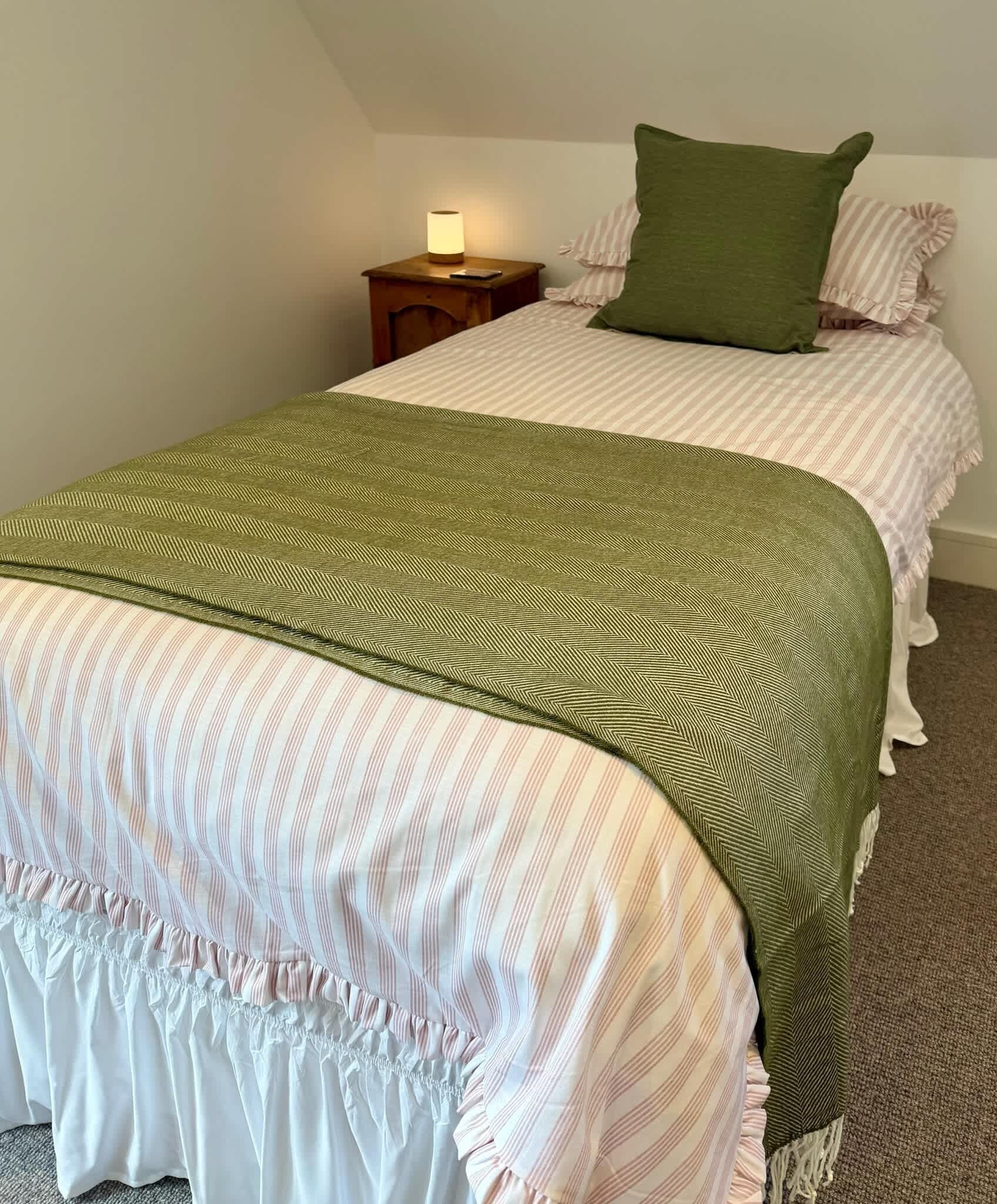 Een tweepersoonsbed met een groen-wit gestreept dekbedovertrek, een groen kussen en een nachtkastje met een lamp.