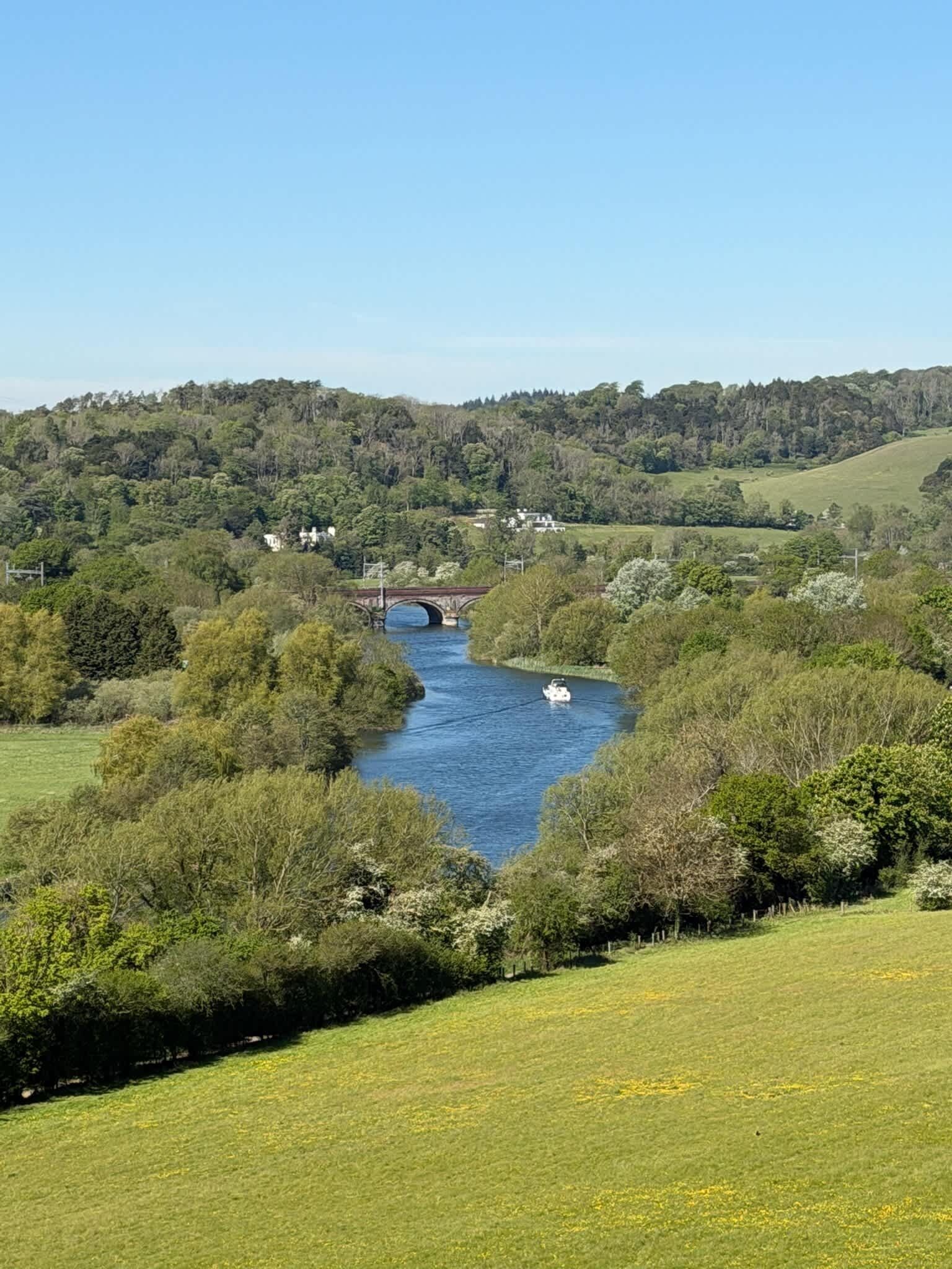 Une rivière traversée par un pont, entourée de verdure et de collines.