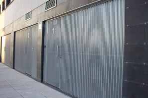 A row of closed metal garage doors with a concrete wall and a tiled sidewalk. - Apartamentos Lumael (Mérida)
