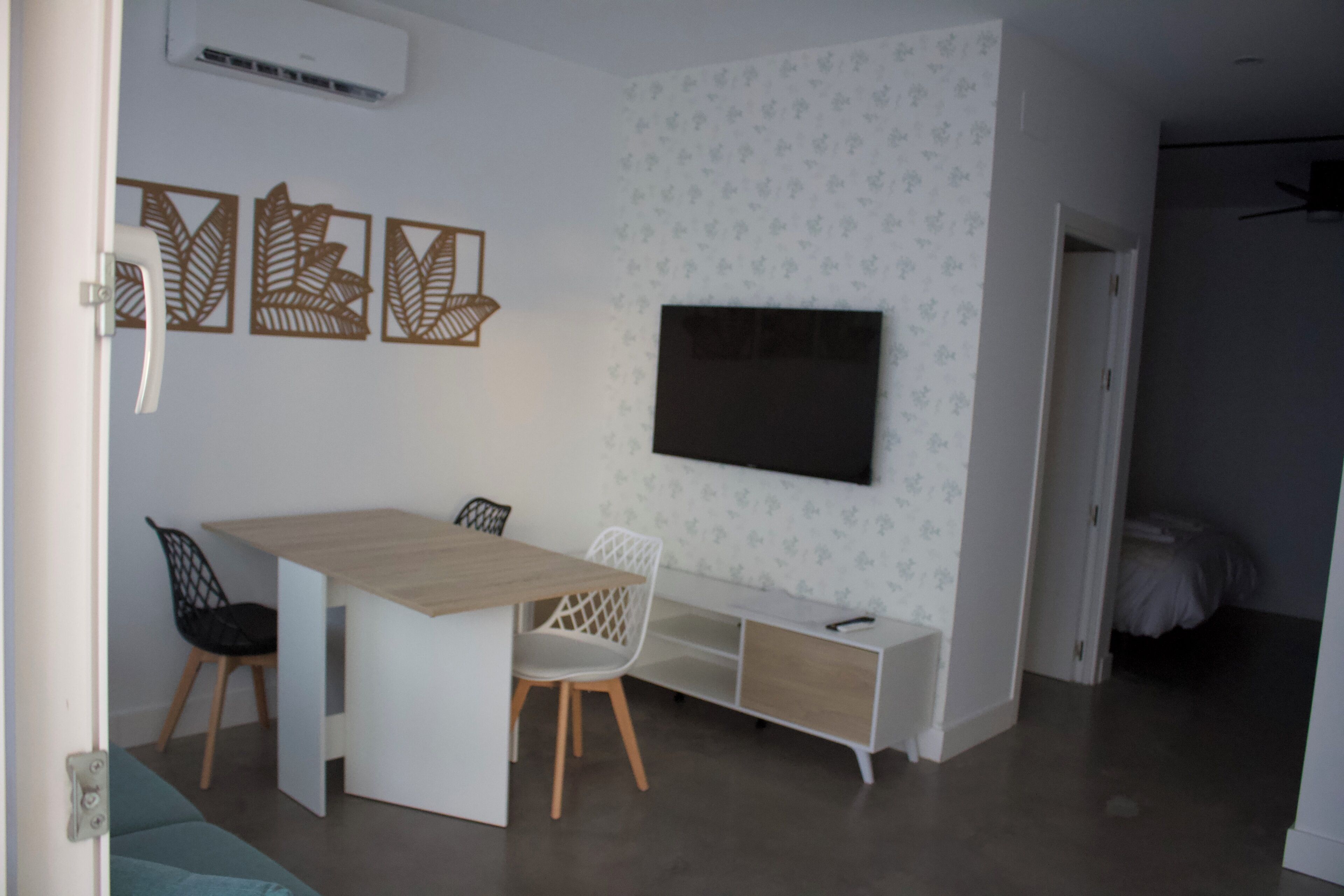 A modern room with a wooden dining table, two chairs, a white cabinet, and a flat-screen TV mounted on the wall.