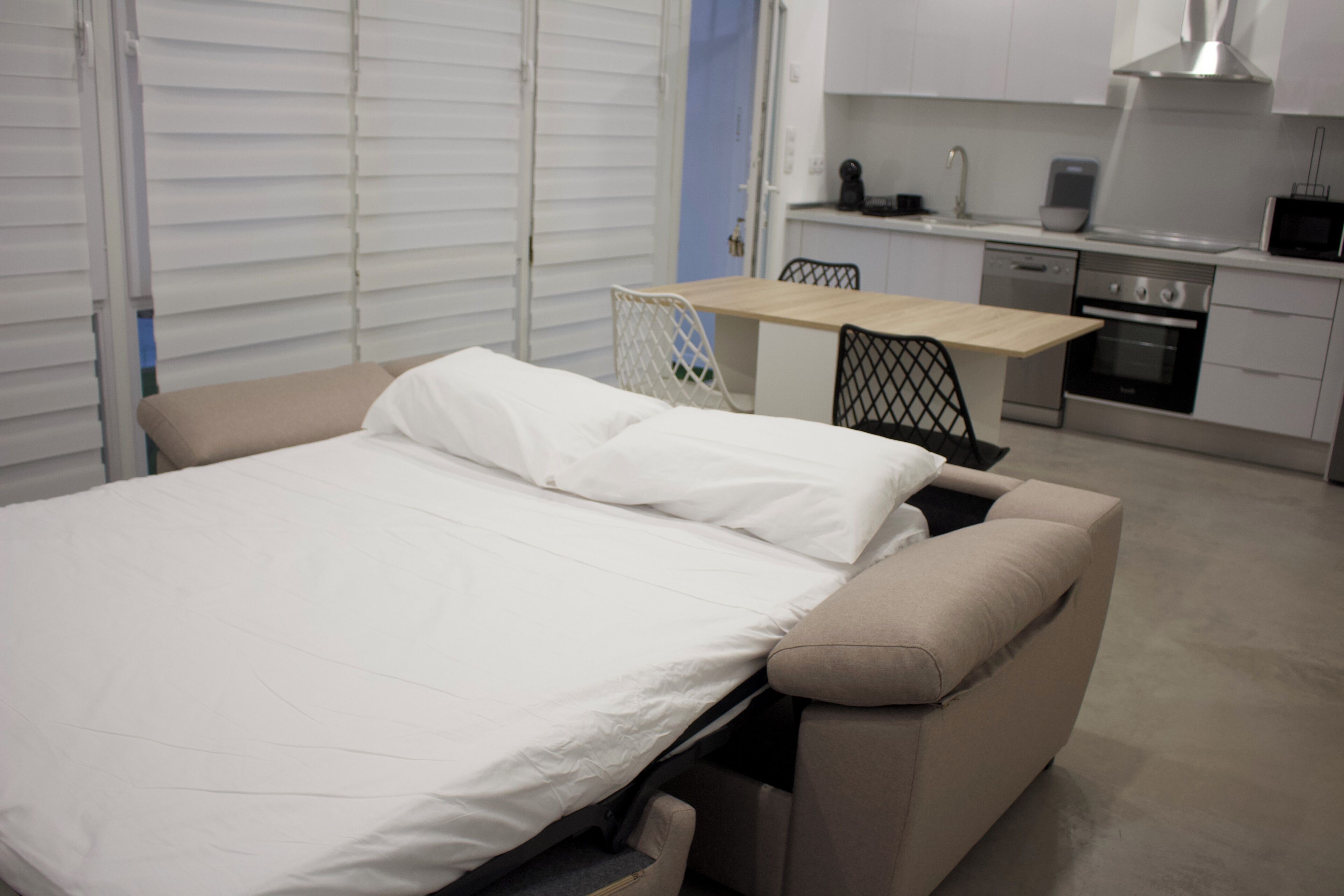 Une chambre avec un lit, une petite table et, au fond, un coin cuisine.