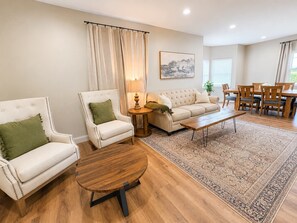 Ein Wohnzimmer mit Sofa, Sessel, Couchtisch und Essbereich mit Stühlen und Tisch.