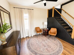 Une pièce avec un escalier, deux chaises, une petite table avec une lampe et un grand tapis.