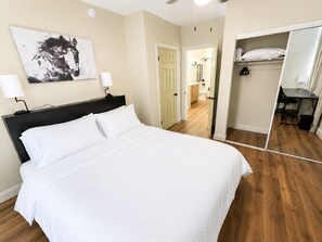 A hotel room with a bed, a nightstand, a lamp, a painting on the wall, and a closet with a mirror. - Spacious 4-bedroom house in quiet Wilmington (Wilmington)