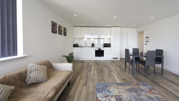 A modern living room with a sofa, a coffee table, and a dining area with chairs and a table. - Modern 2 Bed Apartment in Gravesend w Games Room (Gravesend)