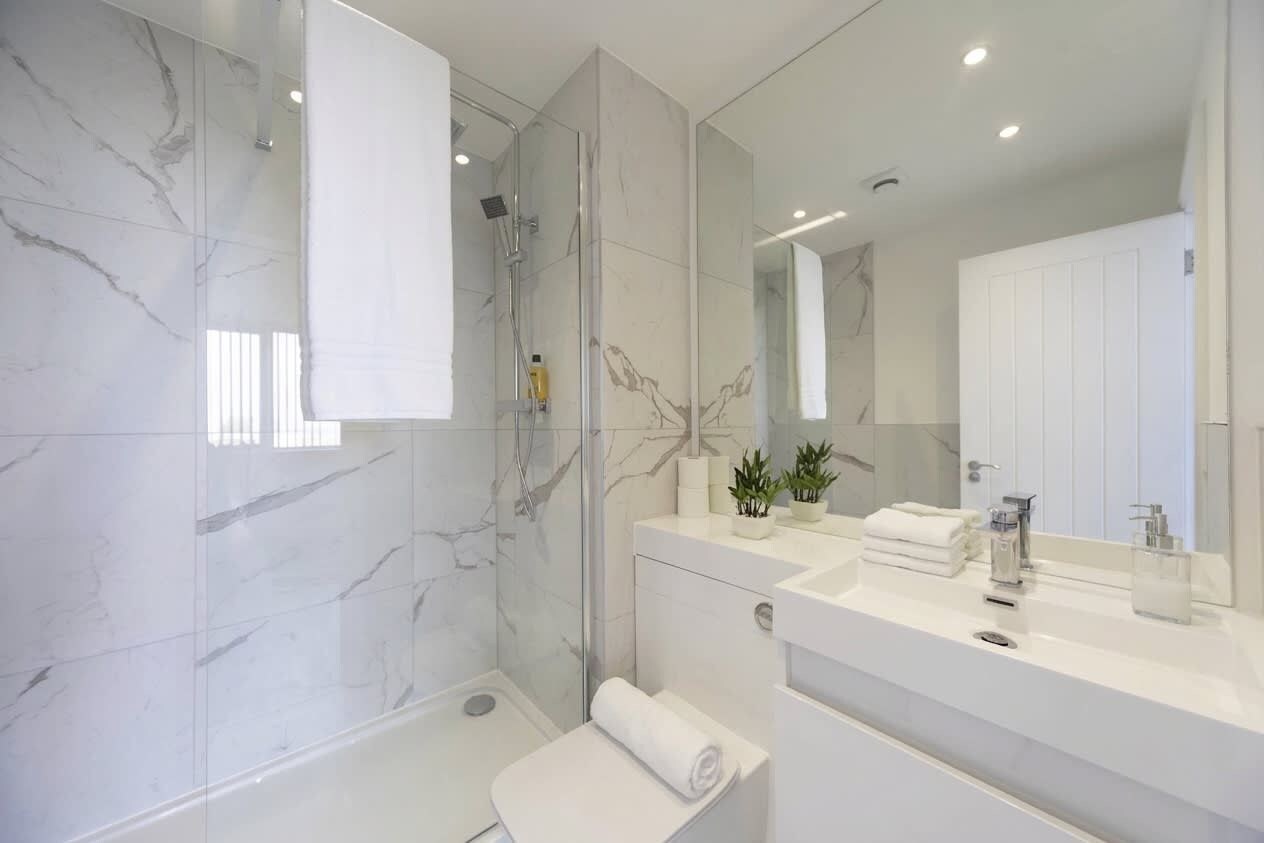 A modern bathroom with a glass shower enclosure, a white sink, and a large mirror.