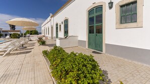 A white building with green doors and windows, a tiled walkway, and outdoor seating with umbrellas. - #361 Quinta Brito Lima D (Paderne)