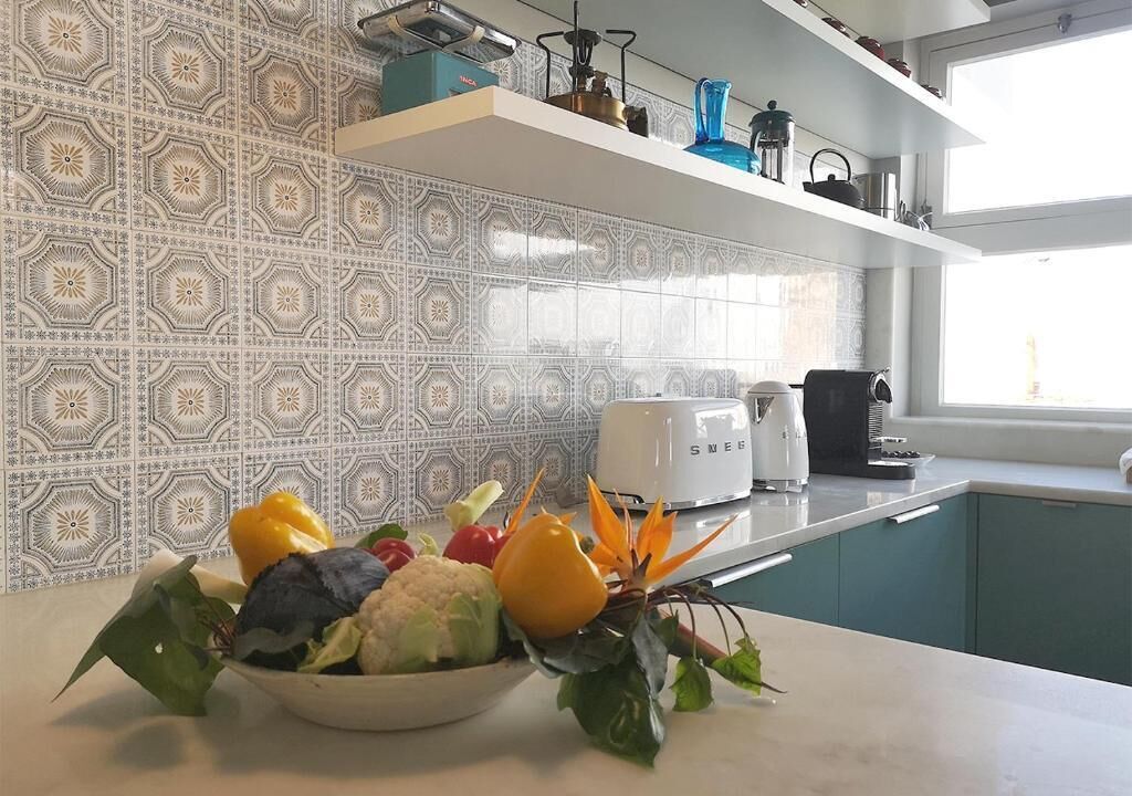 Una cocina con baldosas estampadas, un bol con productos frescos, un tostador y armarios color turquesa.
