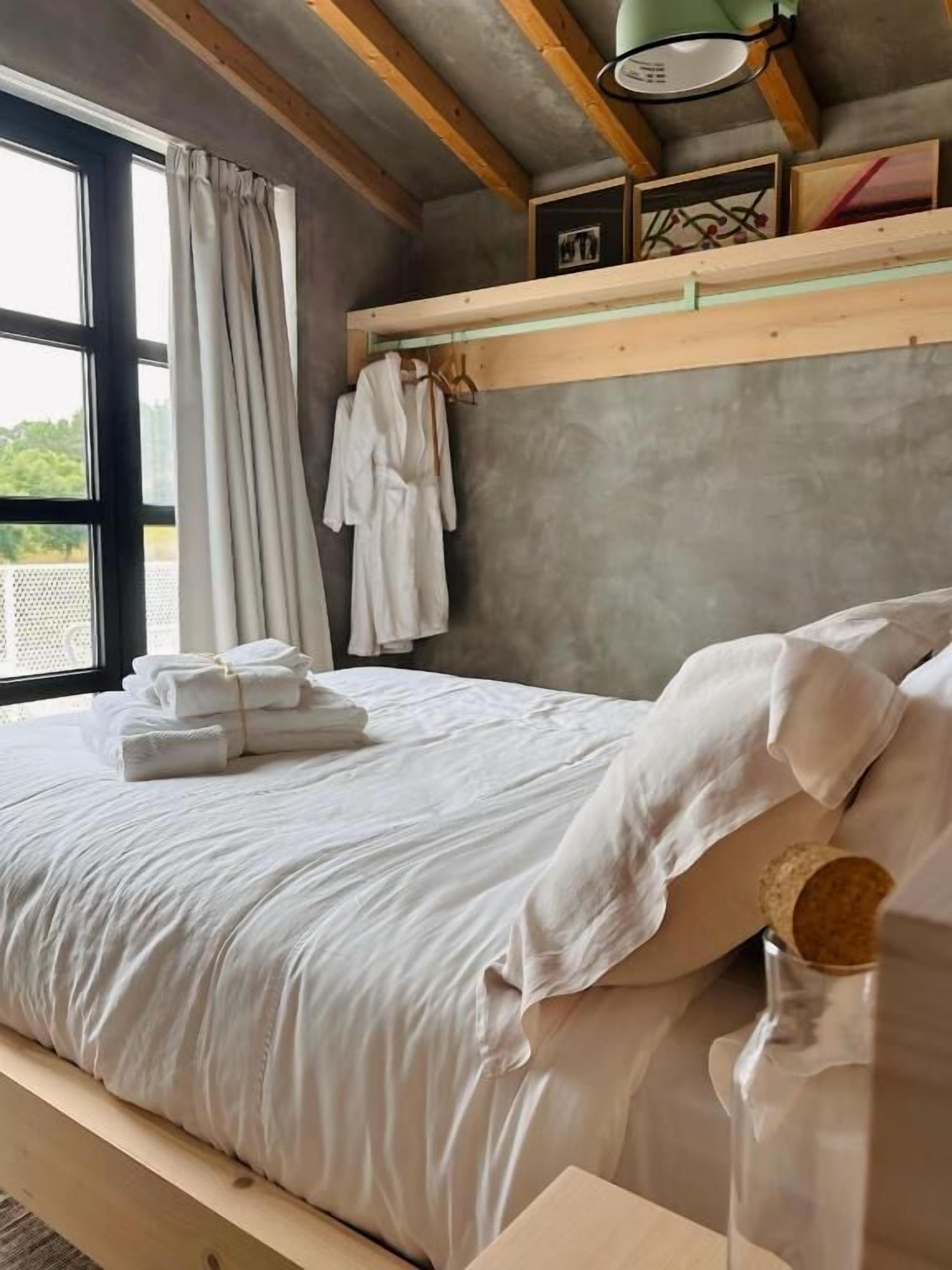 A bedroom with a bed, a bedside table, a hanging robe, and a window with curtains.
