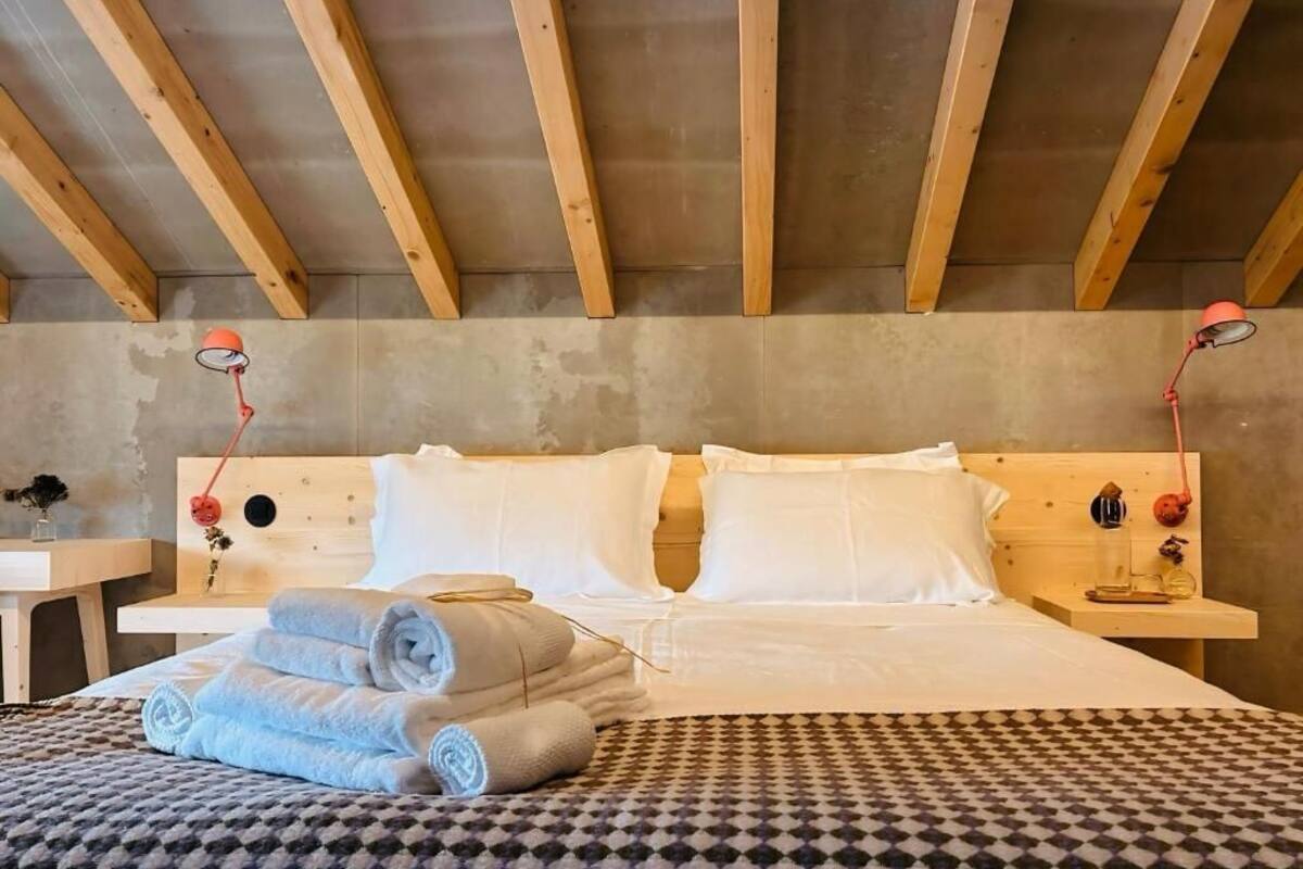 Ein Hotelzimmer mit Holzboden, einem Bett mit weißen Leinentüchern, zwei Nachttischen mit Lampen und einer karierten Tagesdecke.