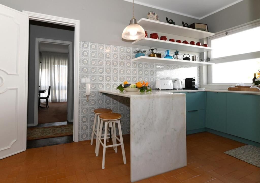 A modern kitchen with a marble island, bar stools, and a pendant light.