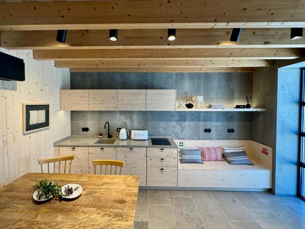 A modern kitchen with wooden cabinetry, a dining table with chairs, and a built-in bench with cushions.