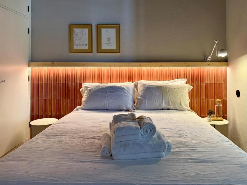 Ein Hotelzimmer mit einem Bett, zwei gerahmten Bildern an der Wand, einer Nachttischlampe und einem zusammengerollten Handtuch auf dem Bett.