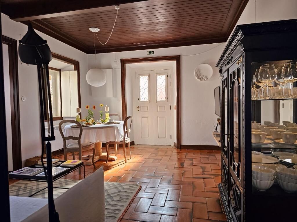 A room with a wooden floor, a dining table with chairs, a white door, and a cabinet with glassware.