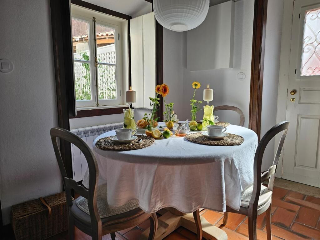 A dining table with a white tablecloth, surrounded by chairs, with a window and a door in the background.