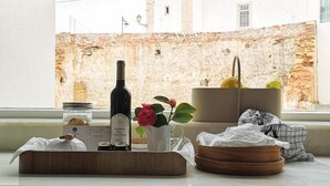 A window view of a historic building with a bell tower, a bottle of wine, a vase with a flower, and a basket with a cloth. - Casaspensadas (Porto de Mos)