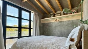 A bedroom with a large bed, a wooden desk, a bottle, and a window with a view. - Casaspensadas (Porto de Mos)