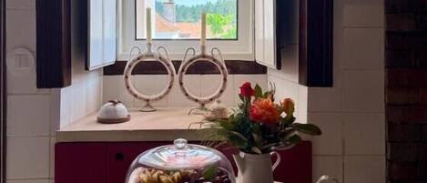 A room with a window, a table with a glass dome, a vase with flowers, and a decorative item on the windowsill.