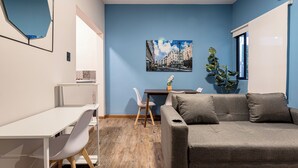 Een kamer met een wit bureau, een grijze bank, een blauwe muur en een stadsgezicht schilderij.