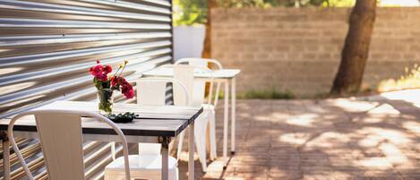 A patio with metal tables and chairs, a brick wall, and a tree in the background.