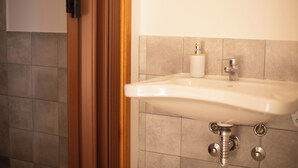 Un bagno con un lavandino bianco, una bottiglia di sapone e una porta in legno.