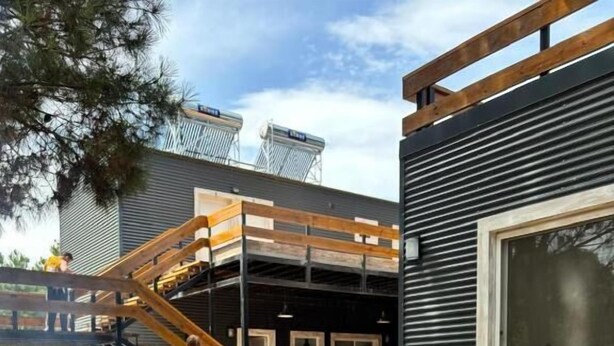 Una griglia barbecue con diversi tipi di carne alla cottura, un patio in legno e un edificio con una finestra e una scala.