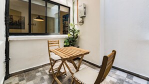 Une petite terrasse avec une table et des chaises en bois, une plante en pot et une fenêtre donnant sur des immeubles.