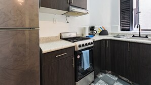 Une cuisine avec des meubles de rangement en bois foncé, une cuisinière à gaz, un four encastré et une fenêtre avec des volets noirs.